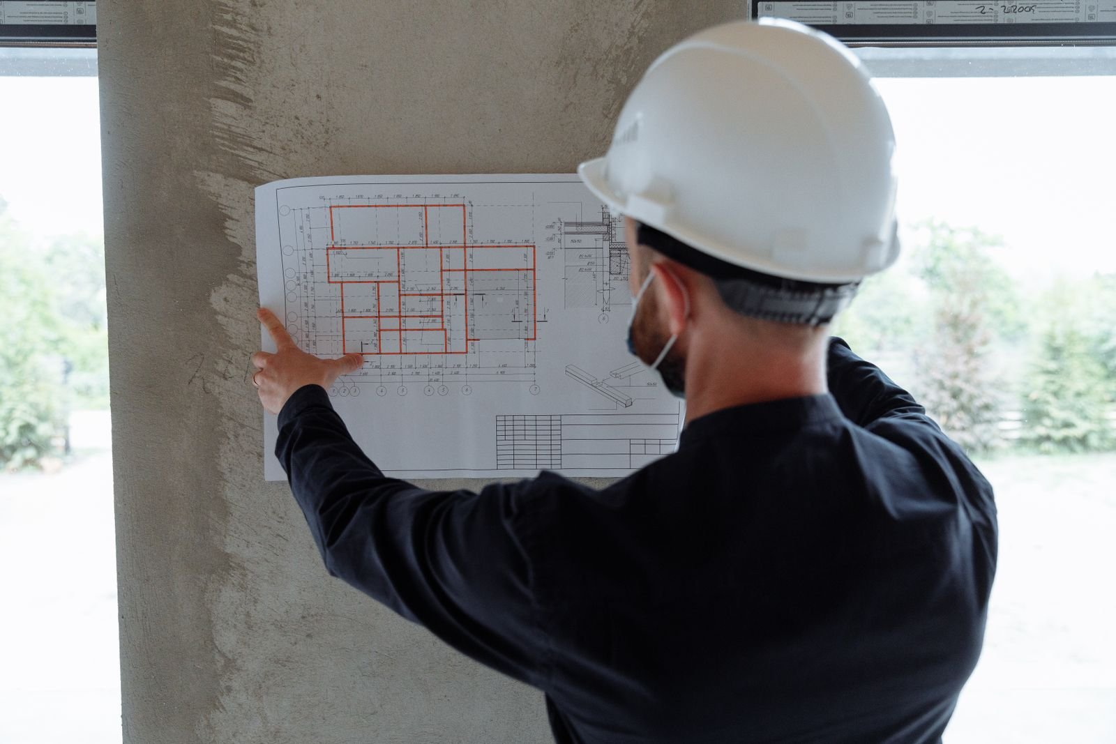 Insinyur berhelm meninjau denah lantai pada kolom beton saat pemeriksaan awal penentuan biaya perkuatan struktur