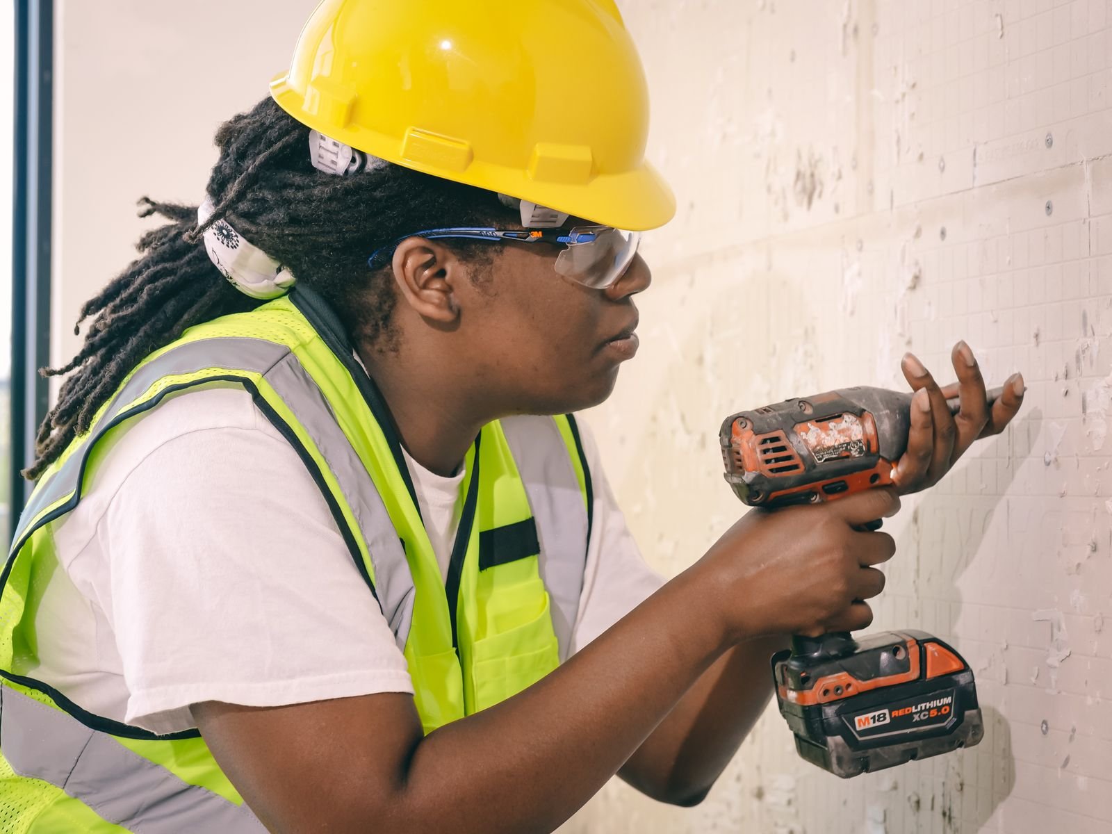 Pekerja dengan helm dan rompi keselamatan mengebor dinding beton, ilustrasi pemasangan packer injeksi epoxy dan PU