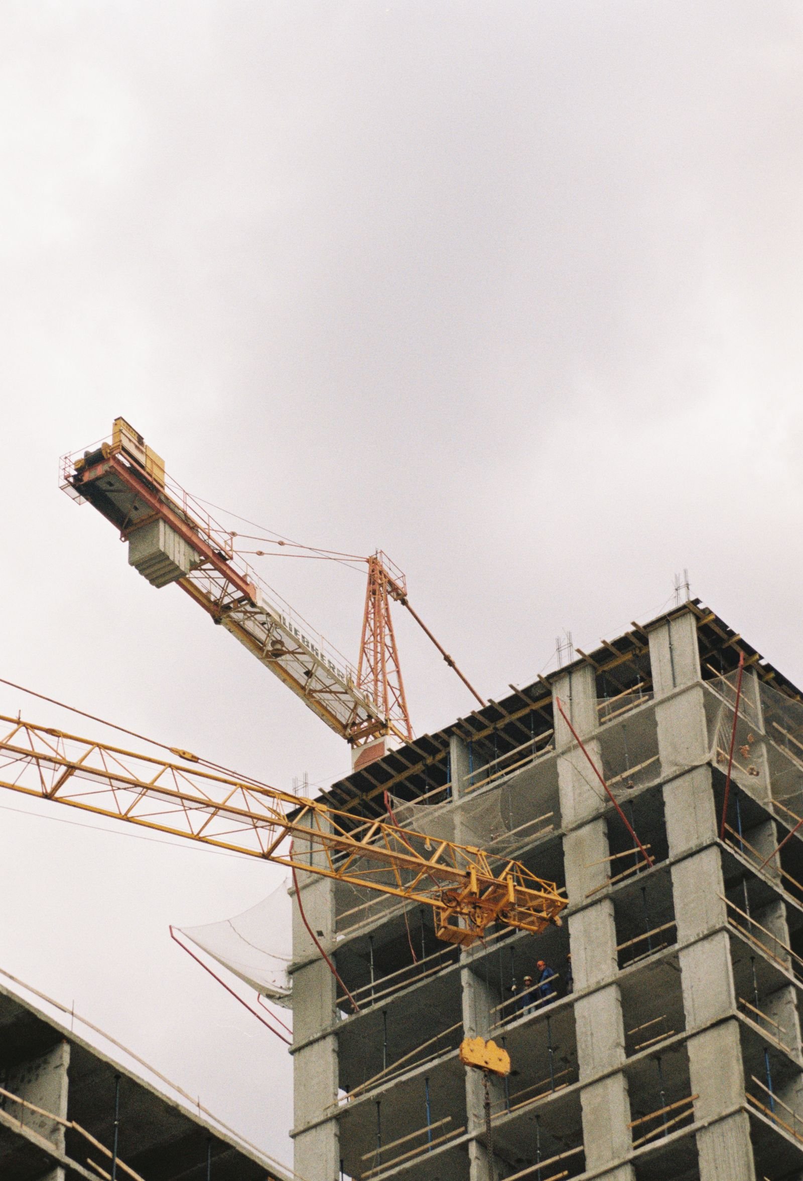 Rangka kolom dan balok beton gedung bertingkat dengan tower crane, ilustrasi skala elemen yang memengaruhi biaya perkuatan struktur